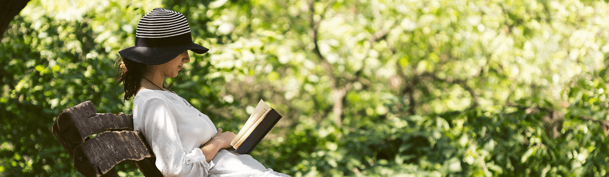 A young woman reads a book in the park under the shade of a tree