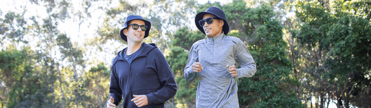 Two young men run in the park wearing sun protective clothing