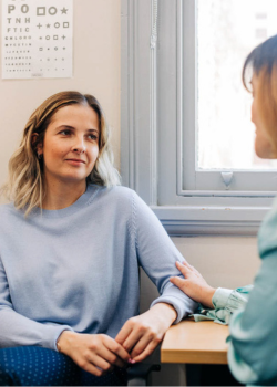 A young woman sits with her doctor speaking about the Cervical Screening Test. Her doctor places a hand on her arm, reassuring her that the test will be easy, quick and comfortable.