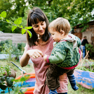 A young mother holding her toddler in a community garden