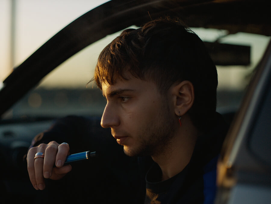 A young man vapes out of his car window, staring into space